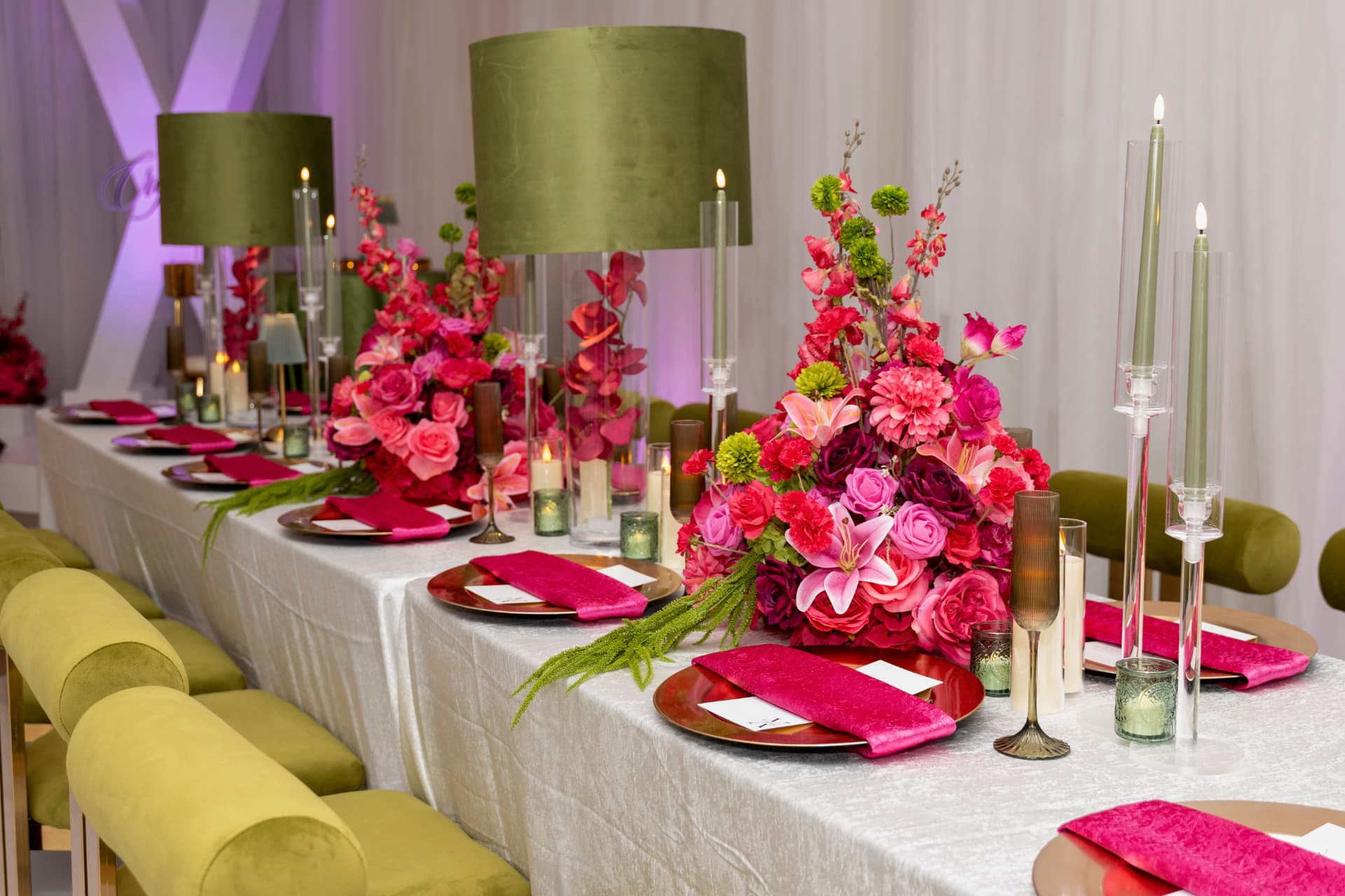 Long guest table with fuchsia napkins, gold chargers, olive lampshades and lush florals