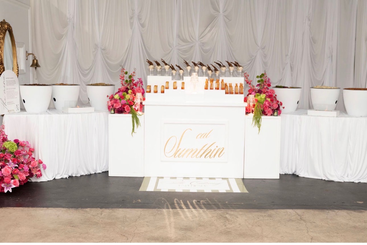 White bar and photo backdrop with calligraphic signage and bright pink florals